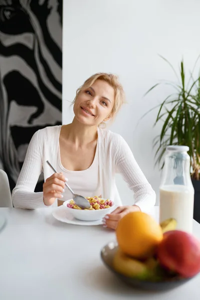 若い女性は家庭のキッチンで健康的な朝食を楽しんでいます 魅力的なスリム女の子食べるボウルのシリアル自家製食品 — ストック写真