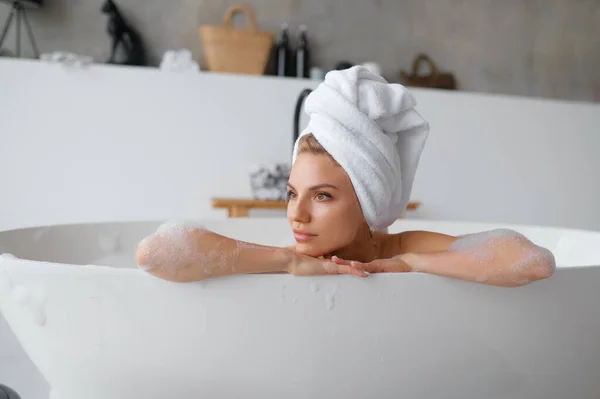 Portrait of gorgeous woman wearing towel on head taking hot aroma bath with foam bubbles. Rest and relax at home day spa concept