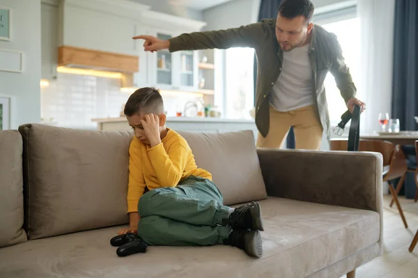 Parenting, video games addiction and discipline in family. Angry father with leather belt shouting on sad unhappy son ready to punish him if boy will play computer video game even more