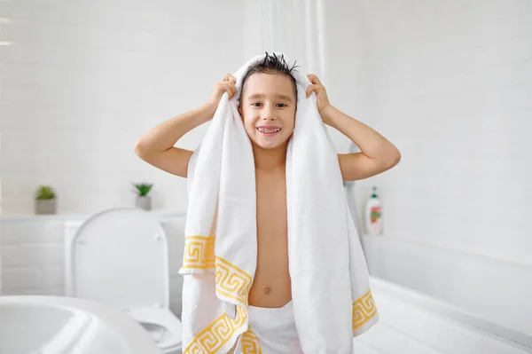 Portrait of happy boy wrapped in white towel showing toothy smile with dental braces after bath or shower. Children morning hygiene routine