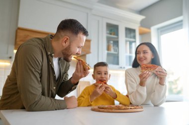 Ebeveynler ve çocuklar rahat evlerinde oturma odasında lezzetli pizzalar yiyorlar. Fast food atıştırmalıkları ve mutlu aile.
