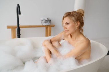 Genç bir kadın ev banyosunda köpük köpükleriyle banyo yapıyor. Milenyum dişisi küvette dinleniyor.