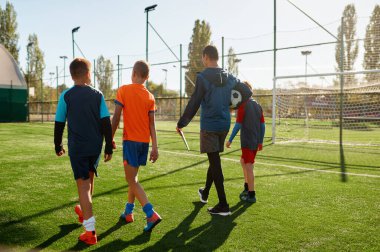 Yakışıklı koçun ve genç futbol takımının sahada yürüdüğü boy portresi. Arka plan