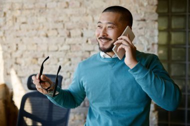 Young businessman talking mobile phone with client in office at coworking center