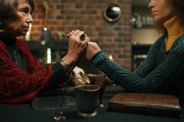 Mature fortune teller firmly grasped young client hands closeup. Old witch saw something terrible on female palms and warning girl