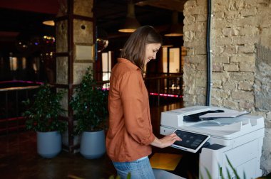 Young woman employee using printer at coworking office. Businesswoman working in creative agency printing documents