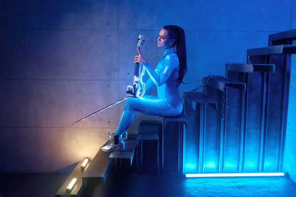 Futuristic concert of young woman violinist in neon light. Beautiful violin player sitting on industrial stairs