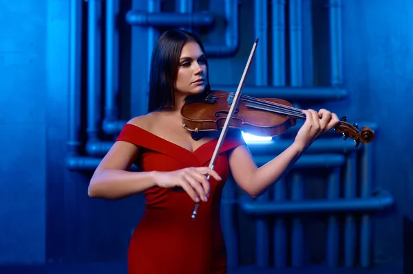 Young pretty woman playing violin solo over loft interior background. Musician playing classical music on musical instrument