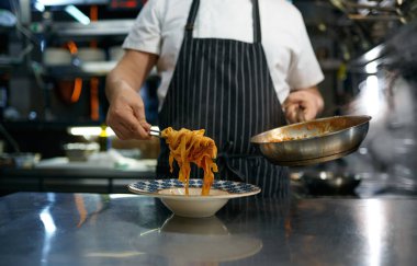 Professional chef serving freshly cooked pasta on plate. Portrait of mature cooker dressed in apron holding spaghetti on fork