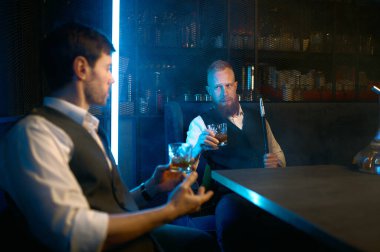 Two young stylish man relax and smoking hookah in bar. Business friends smoke from shisha pipe and drinking in the restaurant