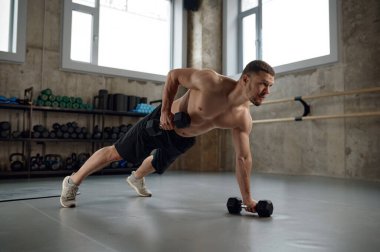 Handsome muscular man doing push ups or standing in wide plank on one arm. Workout training in gym for body building