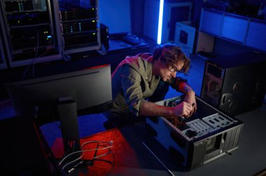 Modern hizmet merkezinde bilgisayar sistemi tamir eden bir adam. Çok çalışan erkek teknisyen gece video kartı montajlarını değiştiriyor