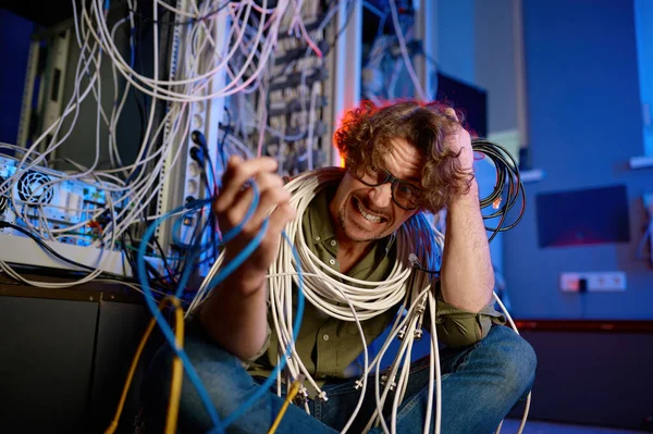 狂ったコンピュータエンジニアは サーバールームのワイヤとケーブルに包まれました インターネット接続を復元しようとして頭の上に髪を引き裂く叫び過労技術サポート労働者 — ストック写真