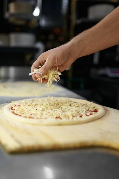 ピザの製造プロセスの概念 閉じられたシェフの手は 新鮮なピザ風にチーズを振りかける — ストック写真