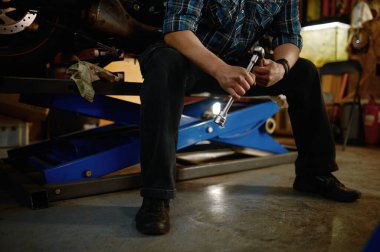 Motorcunun kendi garajında oturup motosiklet tamiri yaptıktan sonra dinlenmesi.