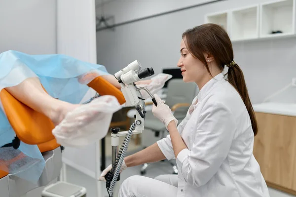 若い医師は婦人科顕微鏡で椅子の上で女性患者の婦人科検査を行う — ストック写真