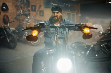 Garaj mağazasında yeni motosiklet deneyen yakışıklı sakallı adam. Motor atölyesinde yeni bir araç seçen motorcu