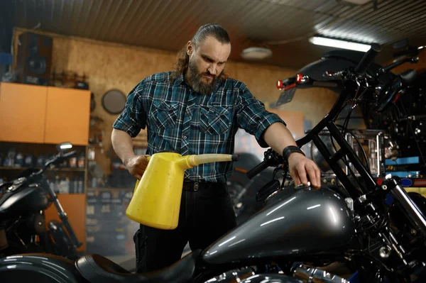 修理作業後にガレージでプラスチック缶から燃料を注ぐ残酷なひげそりの男バイカー給油オートバイ — ストック写真
