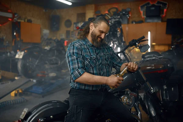 成熟した男バイカーは彼のガレージワークショップで生産的な仕事の後に喜びと満足感ビールを飲む — ストック写真