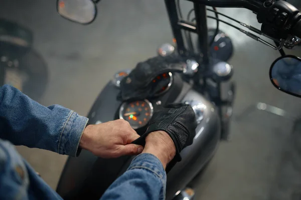 Closeup view on biker hand wearing leather gloves over motorcycle gas tank. Motorbike garage concept