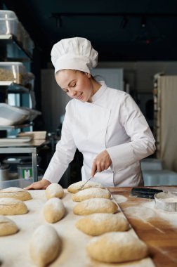 Üniformalı kadın fırıncı geleneksel maya çöreklerini dekore ediyor.