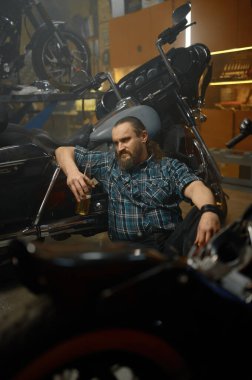 Ciddi bir motorcu yerde oturuyor ve motosikleti tamir etmenin yollarını arıyor. Motosiklet garaj servisi ve hobi konsepti