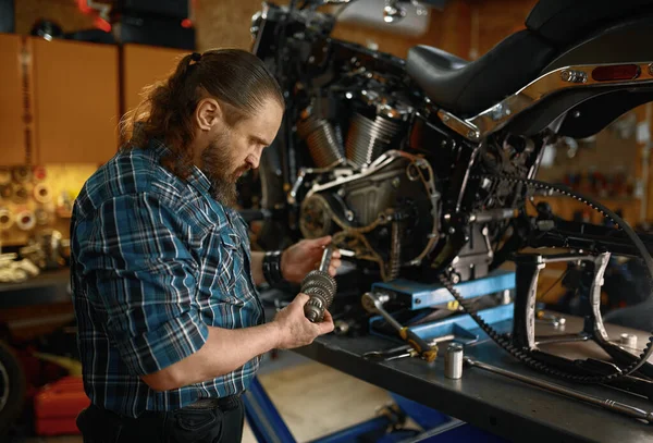 バイクのコンセプトのサービスと修理 バイカー修理工がスペアパーツを見てる 自転車ガレージで働くひげそり成熟した男 — ストック写真