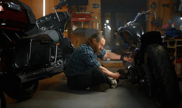 成熟した男バイカーは夜にガレージでオートバイを修理します 仕事中のバイク整備士 — ストック写真