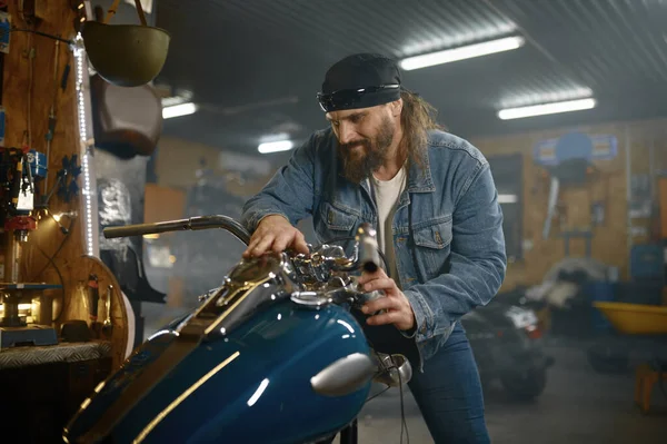 彼の新しいバイクがガレージに立っているのを調べる成熟した男性バイカー ハンサムな髭の男でオートバイ店 — ストック写真