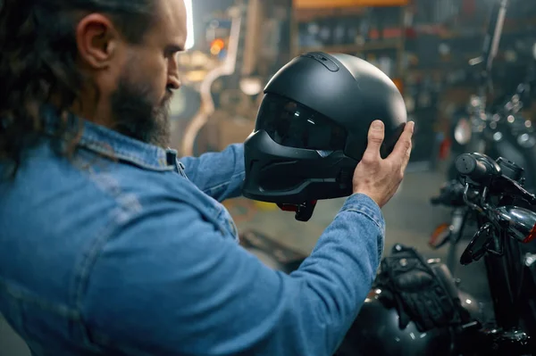 バイクショップで新しい近代的な安全ヘルメットを選択するバイカーにサイドビューショット ガレージ店で乗馬アクセサリーを購入する髭の男 — ストック写真