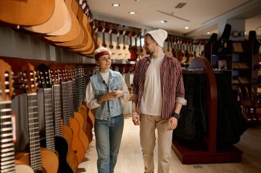 Genç bayan danışman, klasik gitarın nasıl seçileceğini tavsiye eden bir adamla konuşuyor. Müzikal enstrüman dükkanı konseptinde
