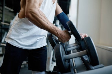 Spor yapan sporcunun spor salonundaki ağırlıklarla egzersiz yapmak için tribünden dambılları çıkardığı kesme bel resmi.
