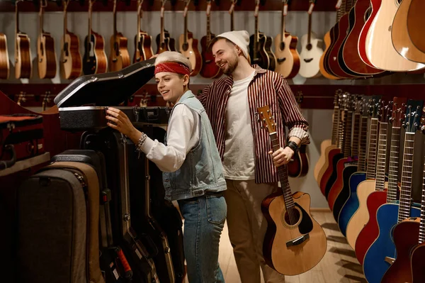 Seller woman helping man buyer to choose guitar case at music shop store. Purchase of new string instrument and accessories