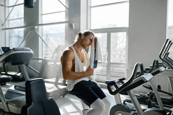 汗びっしょりスポーツマン拭くぬれた額でタオル後ハードトレーニングの楕円形のマシンで現代のジムスポーツクラブ — ストック写真