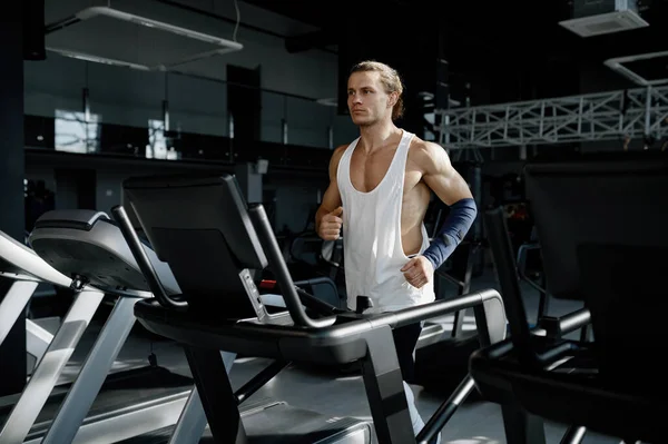 現代のスポーツジムでトレッドミルを走る強い筋肉質の男 カーディオトレーニングを行う固定機械上のアスレチック男性ボディービルダージョギング — ストック写真