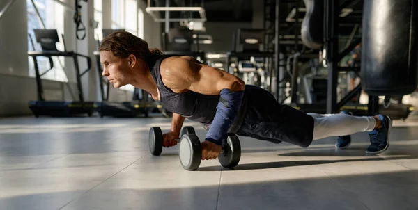 トレーニングジムでダンベルでプッシュアップを行う筋肉の体を持つ強力なボディビルダー スポーツとやる気のコンセプト — ストック写真