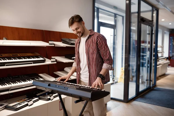 Young hipster man pianist performing at music shop store playing harmony melody on electric piano. Popular musical instrument market