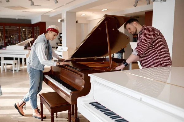 Young musician couple choosing new instrument for family band. Hipster man and woman pianist examining piano at modern music shop store