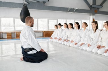Aikido ustası genç kız öğrencilerin önünde oturuyor. Bir grup genç kız için ders başlıyor. Spor salonunda dövüş sanatları eğitimi.