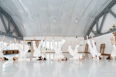 Dövüş sanatları tekniği uygulayan bir grup spor öğrencisi. Kimono giyen genç bir kadın aikido dersi sırasında takla atıyor. Spor ve egzersiz eğitimi.