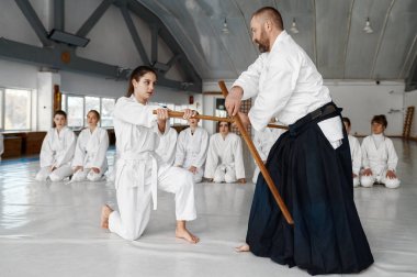 Genç bayan öğrencilerle ahşap kılıçla dövüşen usta bir grup genç kadın savaşçıya aikido yeteneğini gösteriyor.