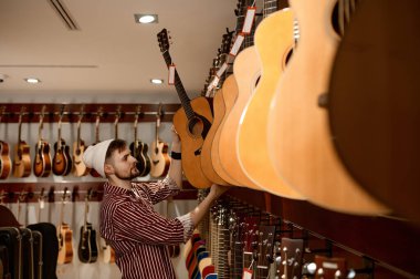 Müzikal enstrüman dükkanının genç erkek sahibi vitrine gitar koyuyor. Küçük işletme ve ticaret kavramı