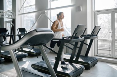 Modern spor salonunda koşu bandında koşan güçlü kaslı adam. Atletik erkek vücut geliştirici, kardiyo eğitimi için sabit makinede koşuyor.