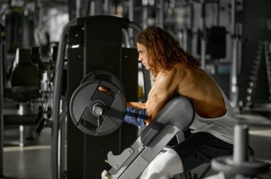 Strong man bodybuilder pumping muscles working with barbell on Scott bench at gym clipart