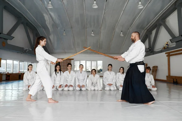 武道のマスター木製の剣と戦うために若い学生を教える 戦いと学習を見ている女性のティーンエイジャーのグループ — ストック写真