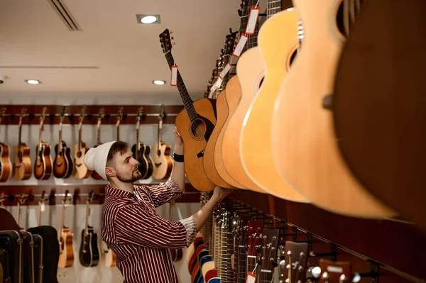楽器店の若い男性オーナーがギターを展示ケースに入れています 中小企業 商取引の概念 — ストック写真