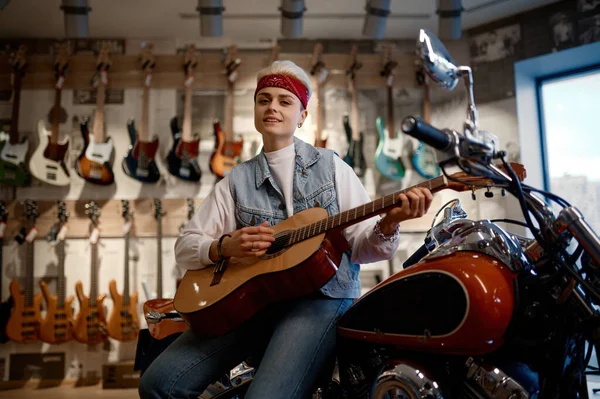 若い女性ロッカーはバイクの上に座って音楽店でギターを演奏します 店の顧客のための創造的なヒップスター女性のロックスター — ストック写真