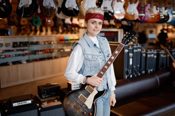プロの音楽店の上に立ってカメラを見て顔に電動ギターと笑顔で若いヒップスター女性ミュージシャンの肖像画 — ストック写真