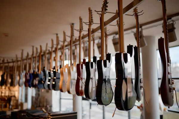 現代音楽ショールームでエレキギターラックに焦点を当てます 購入者を待っている天井に吊るされた弦楽器 — ストック写真