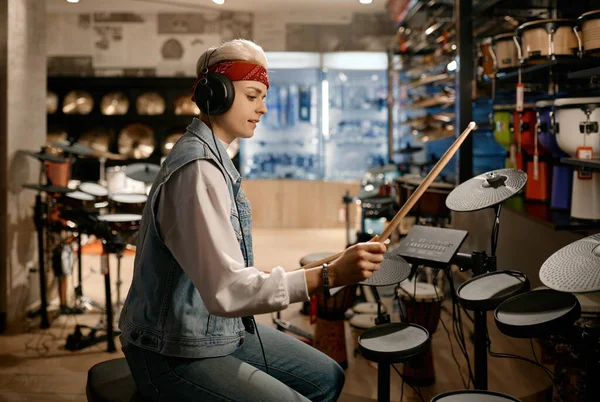 楽器店で電子ドラムセットを演奏するヘッドフォンを身に着けている若いヒップスター女性ミュージシャン — ストック写真